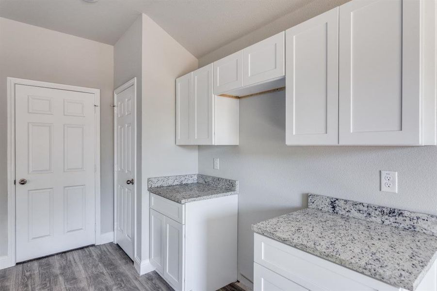 Kitchen with white cabinetry, wood finished floors, and light stone countertops