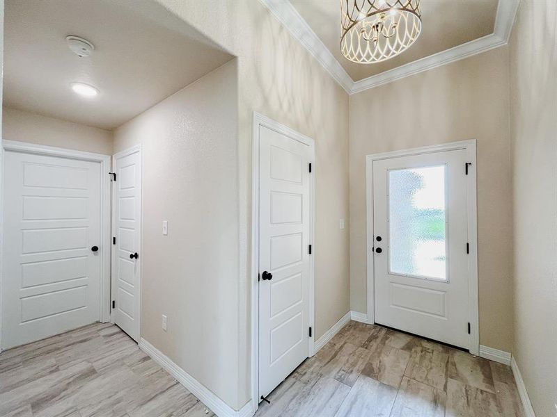 Foyer entrance with light wood-style floors, a chandelier, and ornamental molding Foyer entrance with light wood-style floors, a chandelier, and ornamental molding