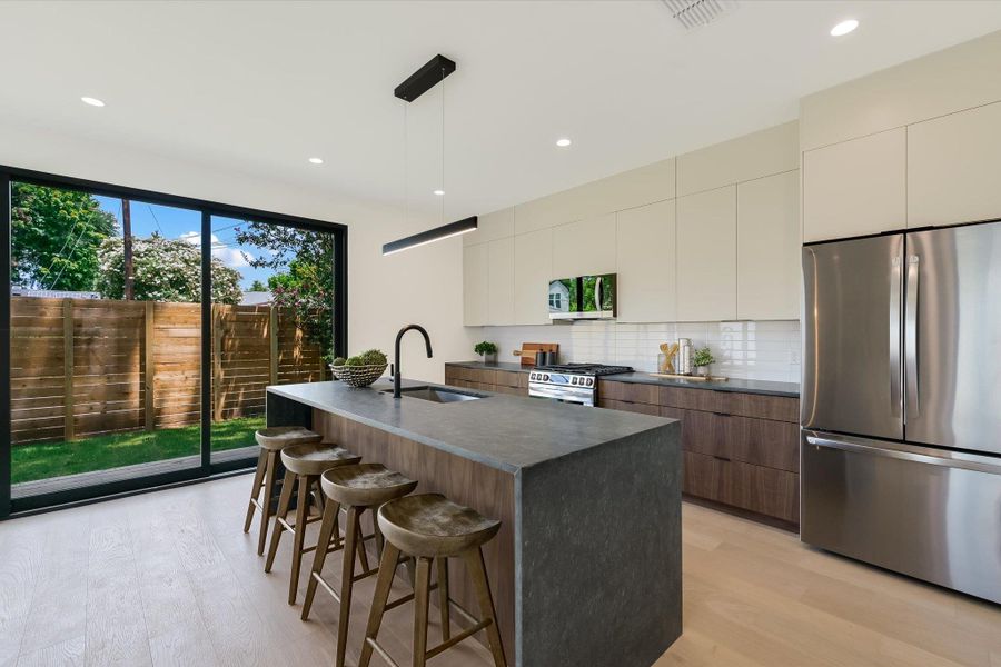 Kitchen with appliances with stainless steel finishes, modern cabinets, dark countertops, a kitchen breakfast bar, and light wood-style flooring