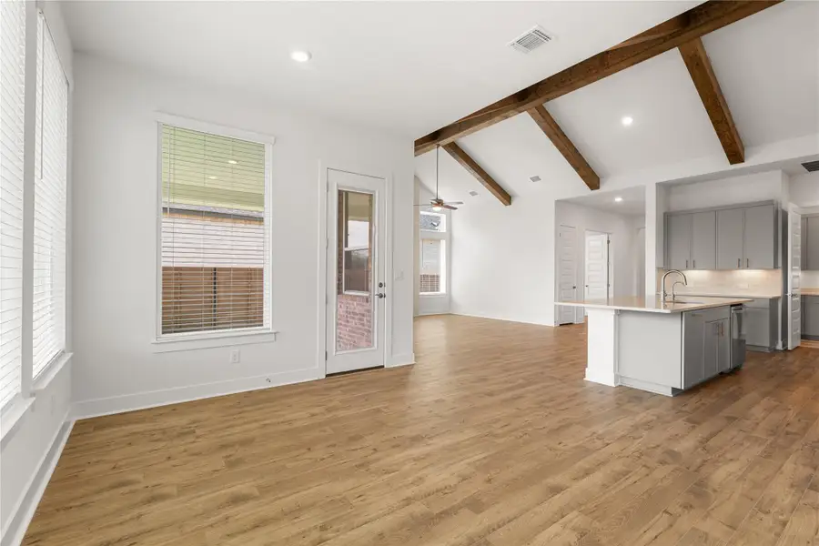 Exposed beams complement wood flooring in this open-concept living space, featuring a kitchen island and natural light. Exposed beams complement wood flooring in this open-concept living space, featuring a kitchen island and natural light.