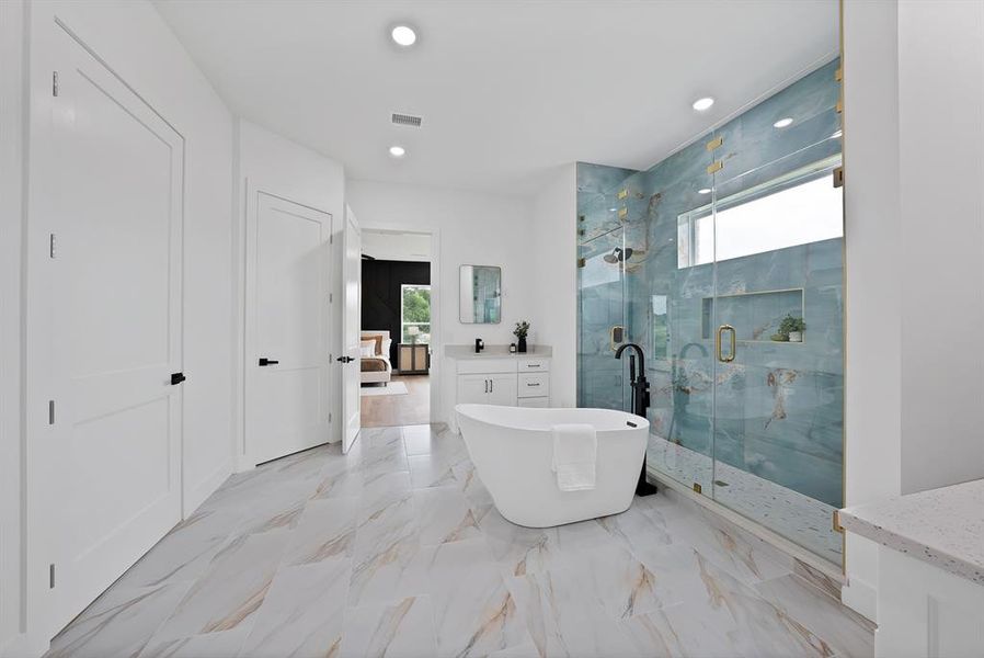Spacious bathroom featuring a freestanding soaking tub, a large glass-enclosed shower with blue-toned tile, a single vanity with stone countertop, and marble-look flooring
