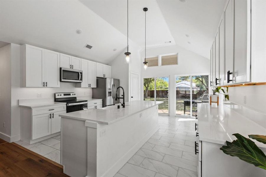 Kitchen with white cabinets, high vaulted ceiling, appliances with stainless steel finishes, decorative light fixtures, and light marble finish flooring