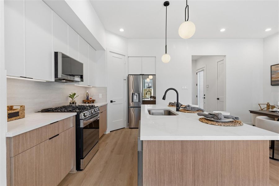 A large island with a white quartz contertops serves as the room’s anchor. Matte black fixtures and integrated stainless steel appliances provide a modern, high-contrast finish.