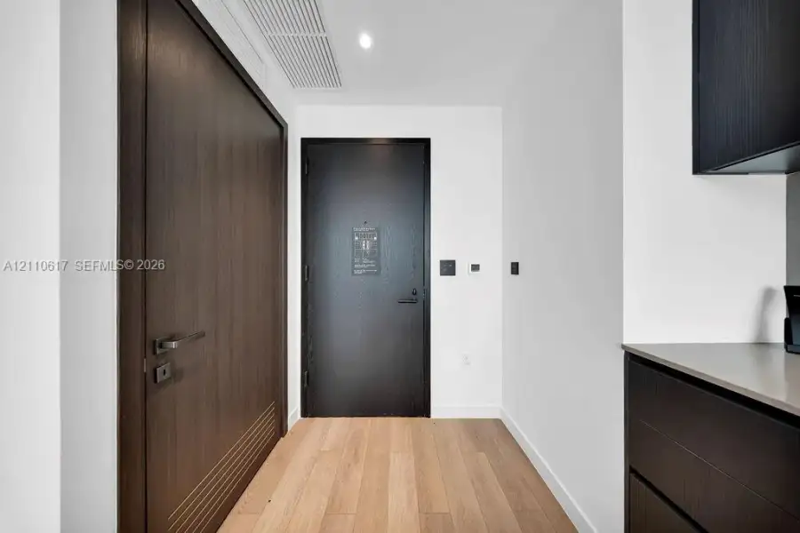 Entryway featuring wood-finish flooring, a matte black door, a full-height dark wood door with horizontal detailing, and modern flat-panel dark cabinetry with a solid surface countertop Entryway featuring wood-finish flooring, a matte black door, a full-height dark wood door with horizontal detailing, and modern flat-panel dark cabinetry with a solid surface countertop
