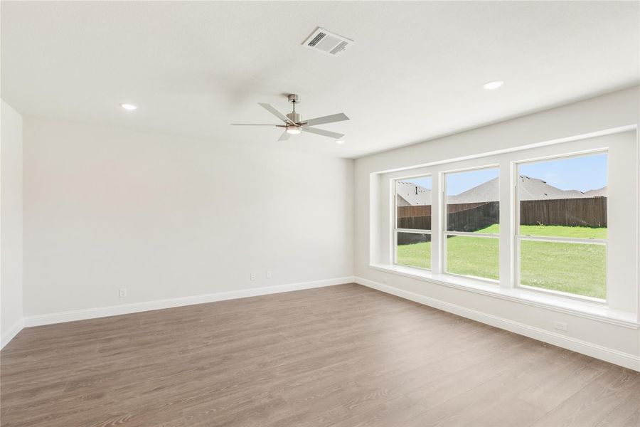 Empty room with hardwood floors, ceiling fan, and large windows overlooking a fenced backyard