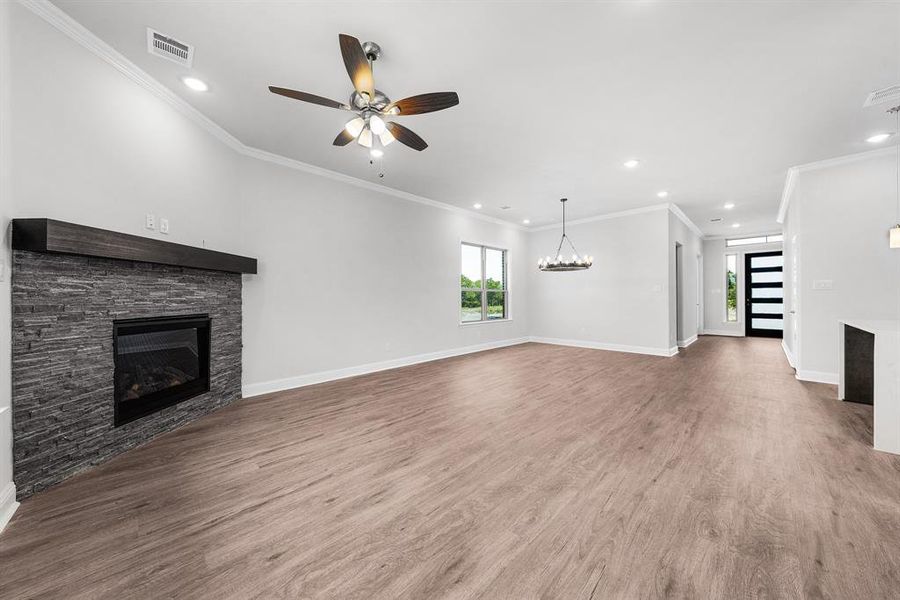 Open living and dining area featuring luxury vinyl flooring, modern chandelier, stained mantel, decorative gas fireplace and recessing lighting. Open living and dining area featuring luxury vinyl flooring, modern chandelier, stained mantel, decorative gas fireplace and recessing lighting.
