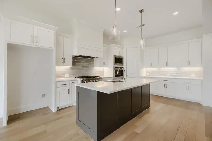 Modern kitchen featuring a dark-toned island with a light-toned countertop, pendant lighting, and wood-finish flooring