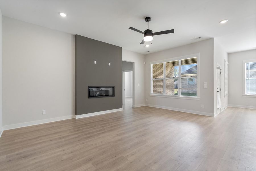 Expansive living area with wood-finish flooring, a modern linear fireplace, and abundant natural light from multiple windows Expansive living area with wood-finish flooring, a modern linear fireplace, and abundant natural light from multiple windows