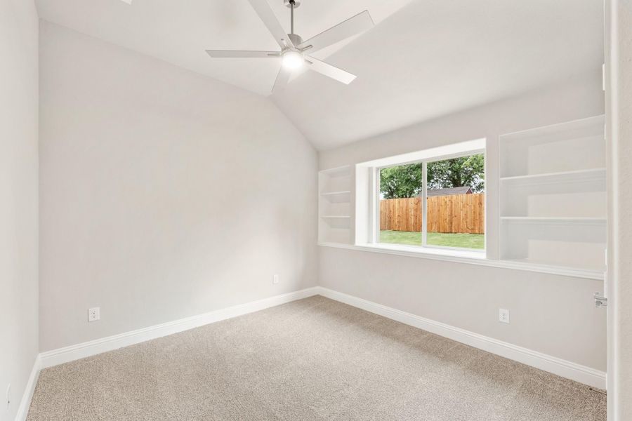 Empty bedroom with vaulted ceiling, ceiling fan, built-in shelves, and carpet flooring
