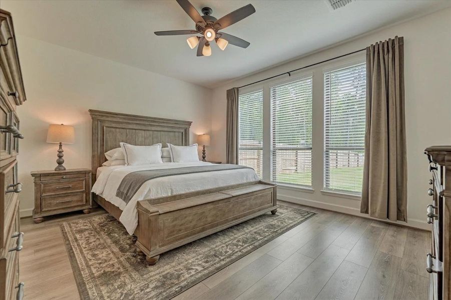 Discover the serene elegance of this primary bedroom, featuring a rustic wooden bed, ample natural light from expansive windows, and a cozy, inviting atmosphere perfect for relaxation.