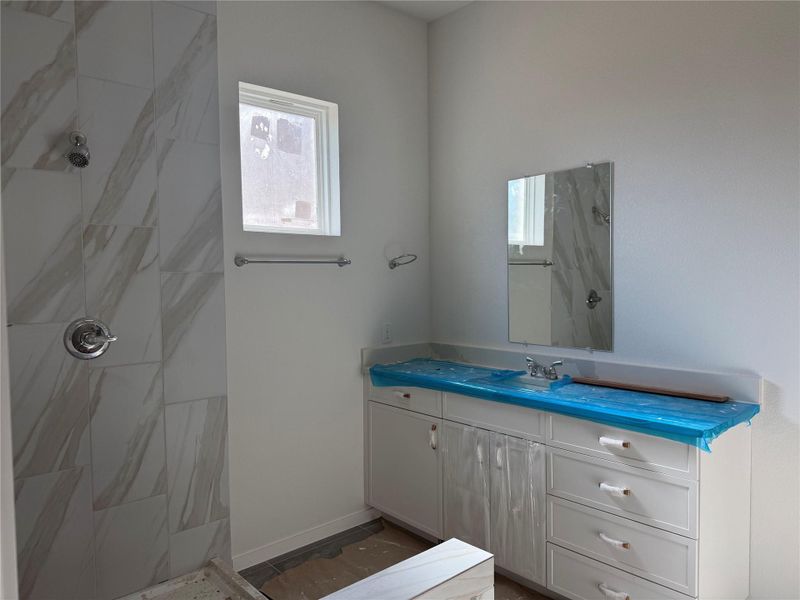 Tiled walk-in shower stands adjacent to a modern vanity under high ceilings.
