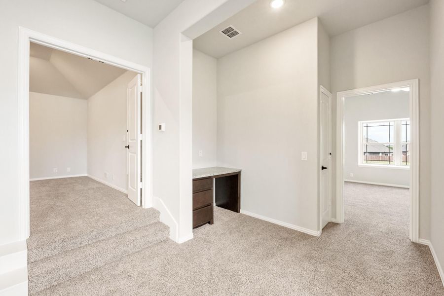 Empty bedroom with carpet flooring, built-in desk, walk-in closet, and door to ensuite bathroom Empty bedroom with carpet flooring, built-in desk, walk-in closet, and door to ensuite bathroom
