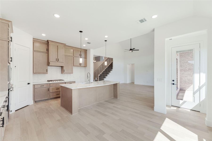 Open kitchen with tan wood cabinets, large center island, white countertops, and light hardwood floors