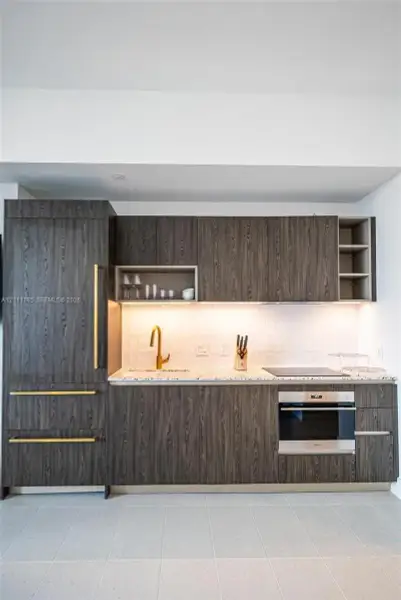 Dark wood-finish cabinetry, brass-toned hardware, stone-composite countertop, integrated refrigeration, and stainless steel wall oven