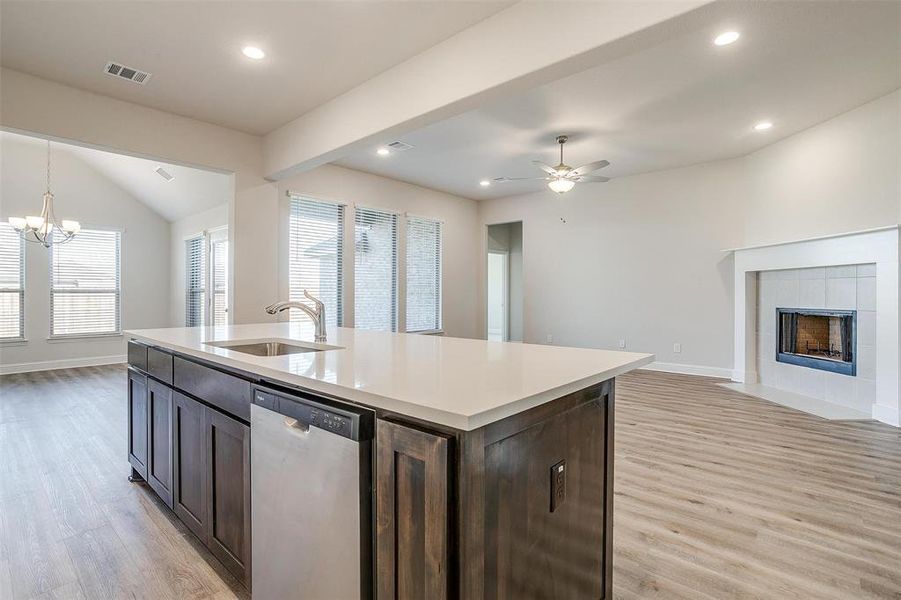 Kitchen with dark brown cabinetry, sink, stainless steel dishwasher, light hardwood / wood-style floors, and a center island with sink