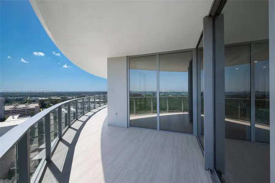 Curved wrap-around balcony featuring large-format tile flooring, glass-panel railing, and floor-to-ceiling sliding glass doors