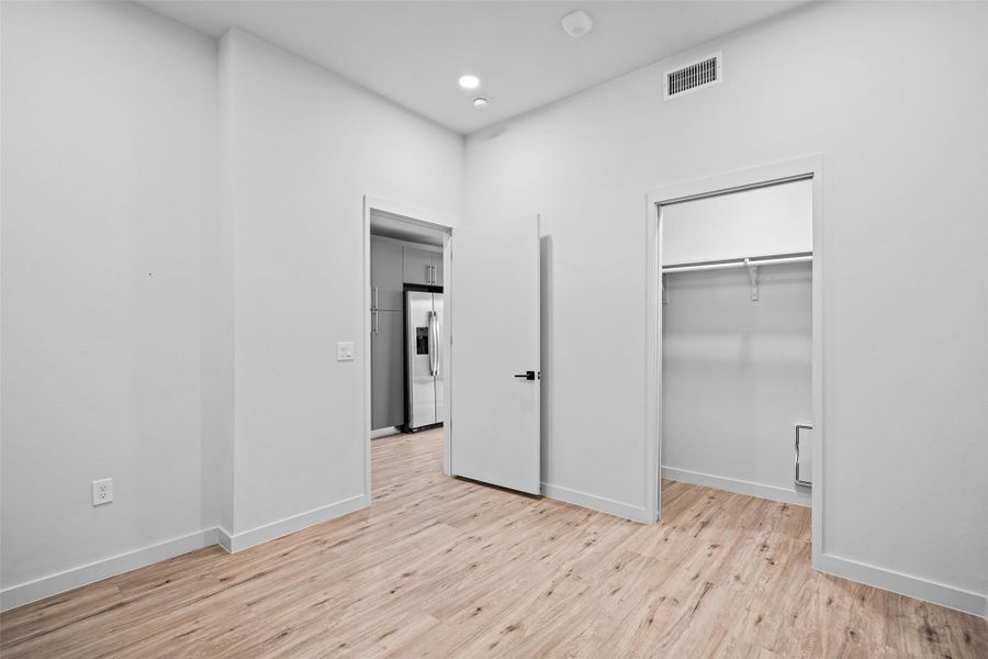 Unfurnished bedroom with light wood-style floors, stainless steel fridge with ice dispenser, visible vents, and baseboards