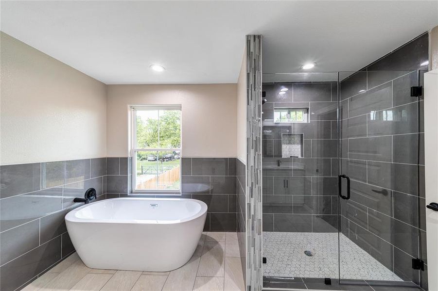 Bathroom featuring tile walls, a stall shower, a soaking tub, wainscoting, and recessed lighting