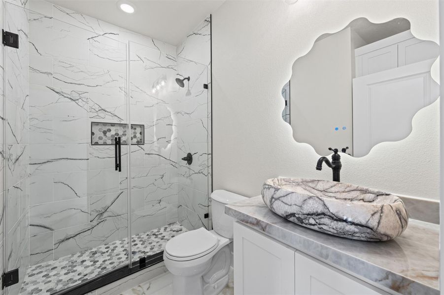 Marble finishes and a glass-enclosed shower elevate this contemporary bathroom design.