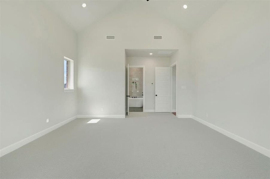Unfurnished bedroom featuring light colored carpet, a high ceiling, recessed lighting, and ensuite bathroom