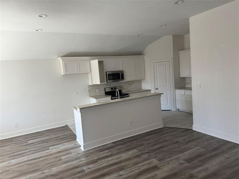 Kitchen featuring wood-type flooring, stainless steel appliances, white cabinets, light stone counters, and vaulted ceiling