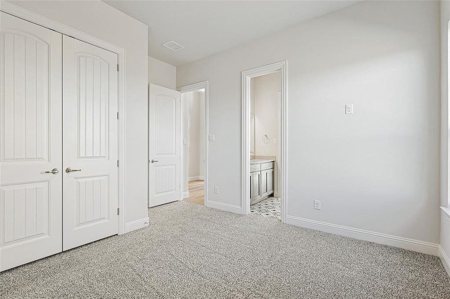 Unfurnished bedroom featuring light carpet, a closet, and ensuite bath
