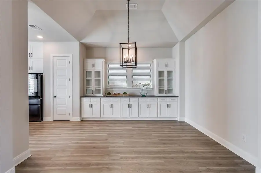 Kitchen featuring white cabinetry, dark countertops, a chandelier, light wood-type flooring, and pendant lighting