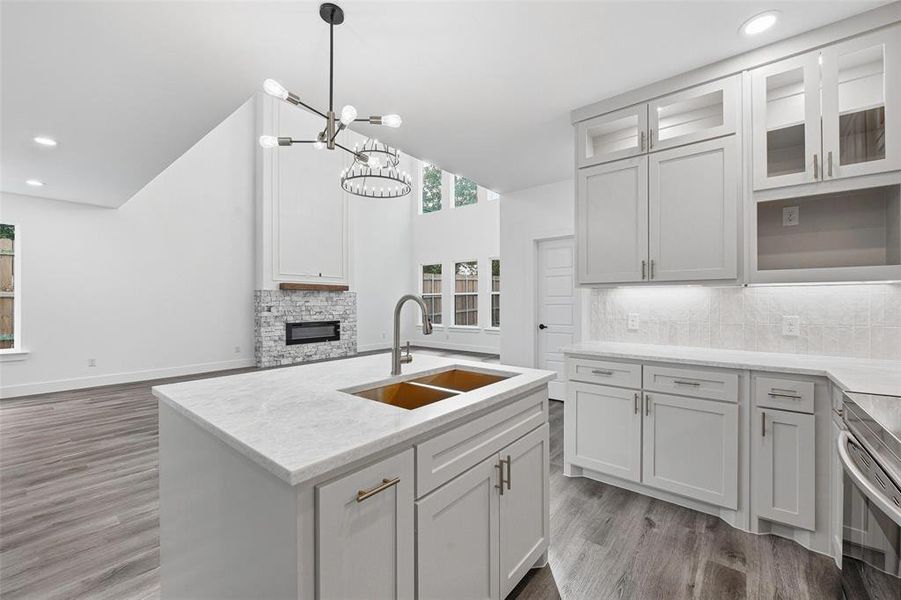 Kitchen featuring recessed lighting, decorative backsplash, a stone fireplace, an island with sink, and glass insert cabinets