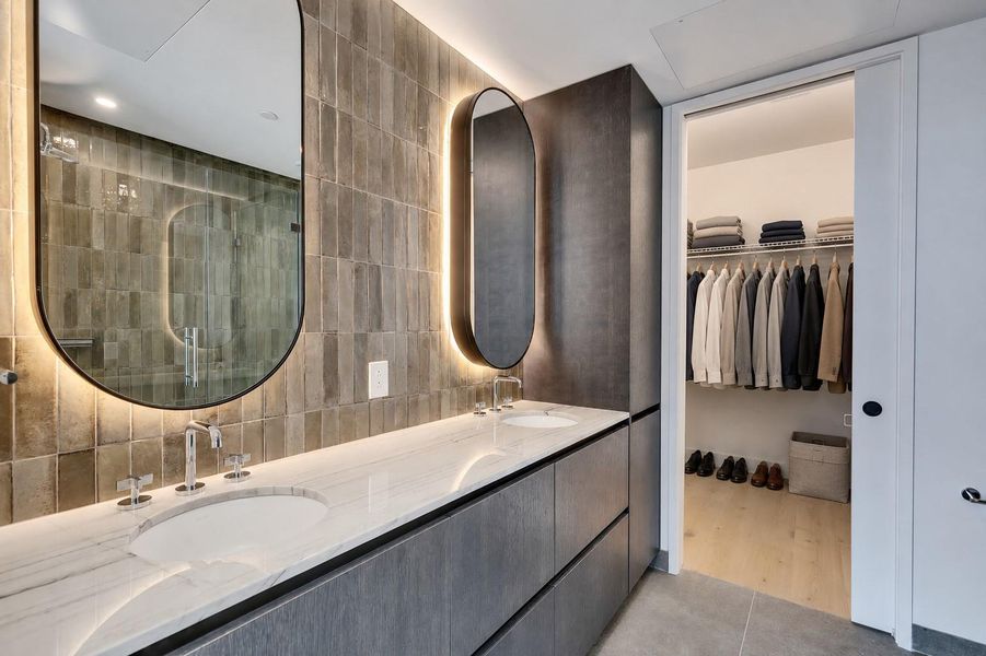 A contemporary double vanity stands adjacent to an organized walk-in closet. A contemporary double vanity stands adjacent to an organized walk-in closet.