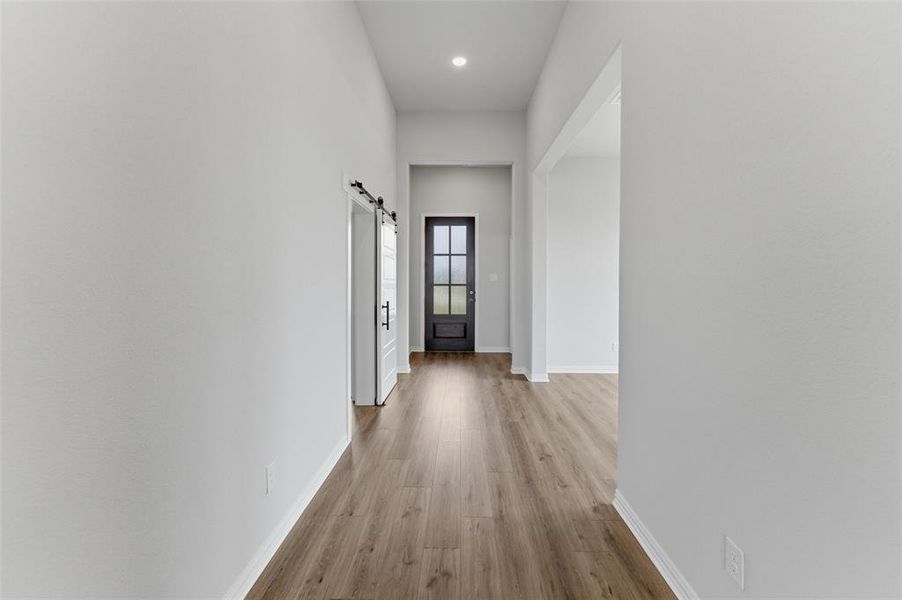 The property features a hallway with light-colored walls, wood-style flooring, and a dark-framed door with glass inserts at its end