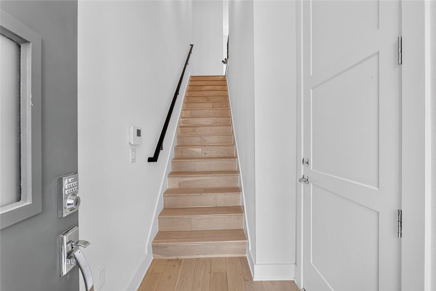 Clean lines and light wood flooring define the inviting entry and staircase of this contemporary residence. The 2-car garage entrance door is on the right.