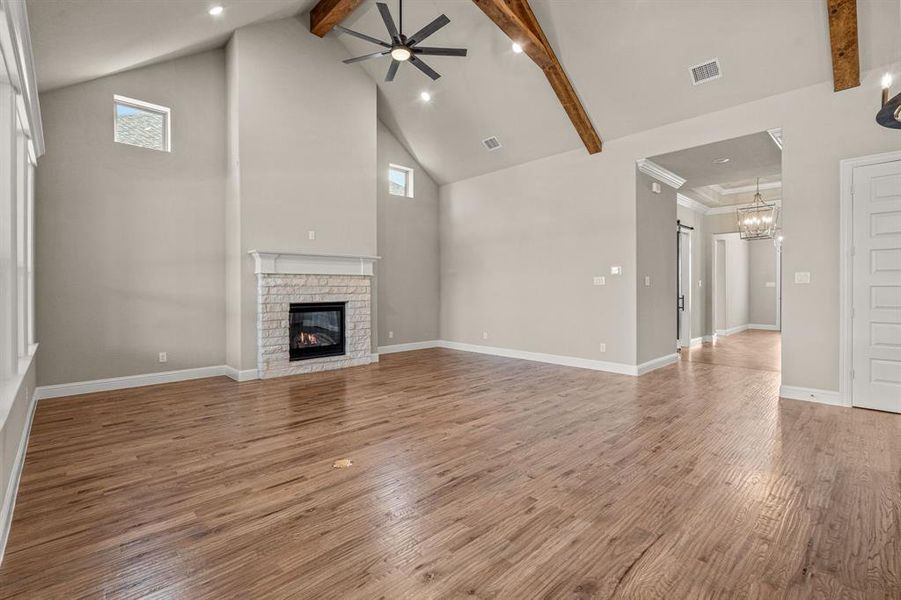 Unfurnished living room with high vaulted ceiling, ceiling fan, beam ceiling, light wood-style floors, and a fireplace