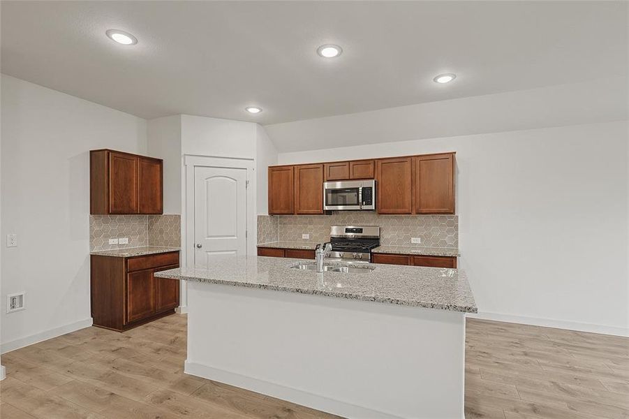 Kitchen featuring backsplash, stainless steel appliances, light wood-type flooring, and a center island with sink