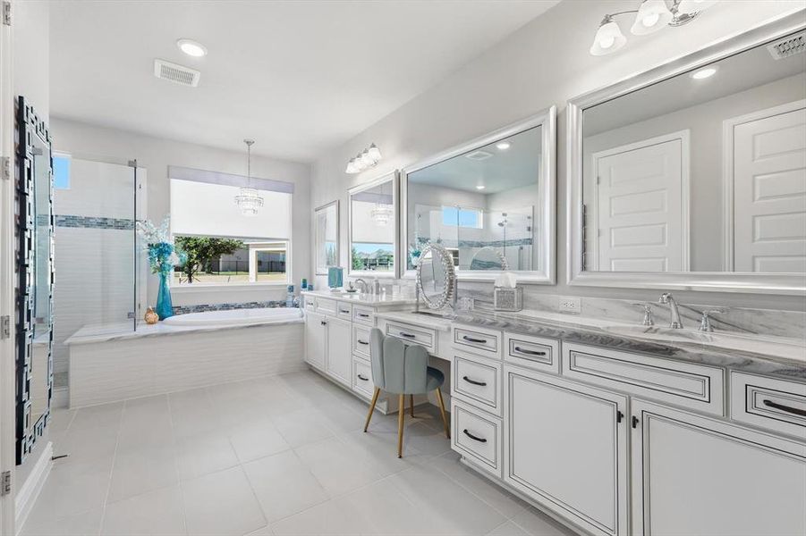 Spacious bathroom featuring a double vanity with stone countertops, an integrated soaking tub, a separate glass-enclosed shower, and a dedicated vanity seating area