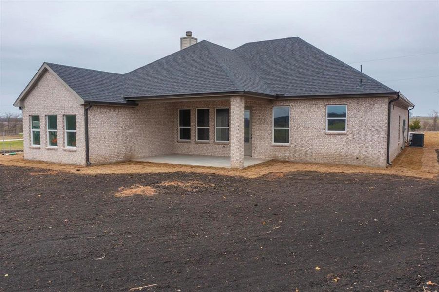 Rear view of house featuring brick siding, a chimney, roof with shingles, and a patio area