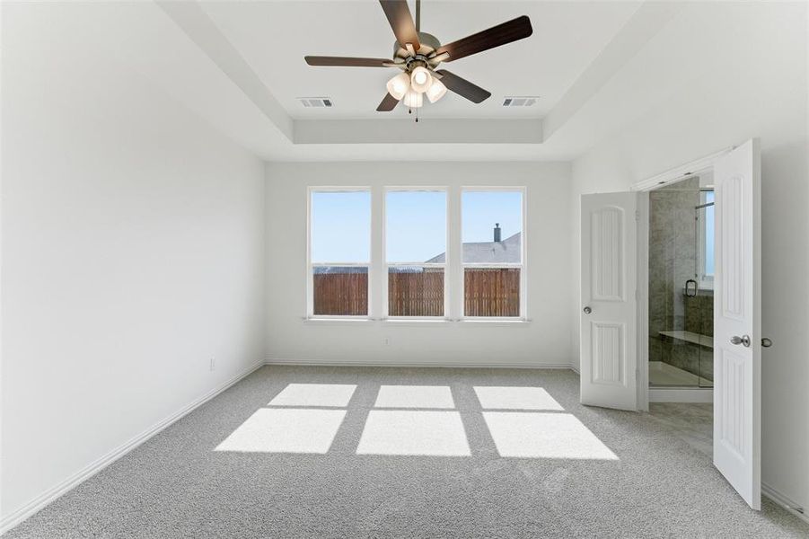 Empty room featuring ceiling fan, light colored carpet, and a tray ceiling