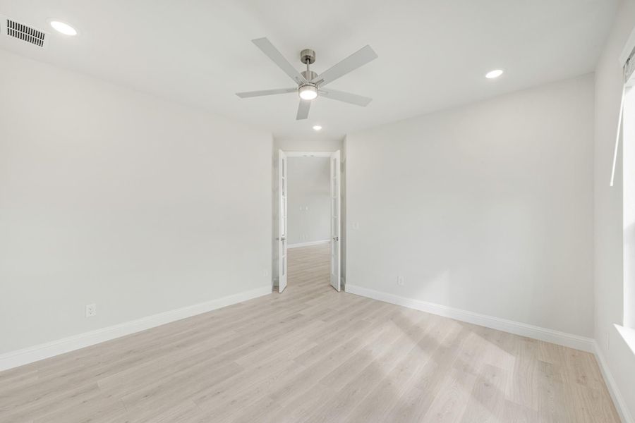 Empty bedroom with light wood floors, ceiling fan, recessed lighting, and open double doors