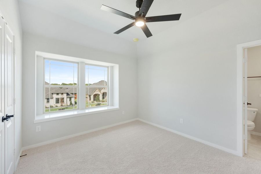 Empty bedroom with carpet, ceiling fan, large window, and attached bathroom doorway