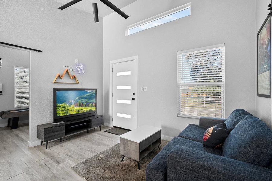 Living room featuring light wood-style flooring, a high ceiling, and ceiling fan.