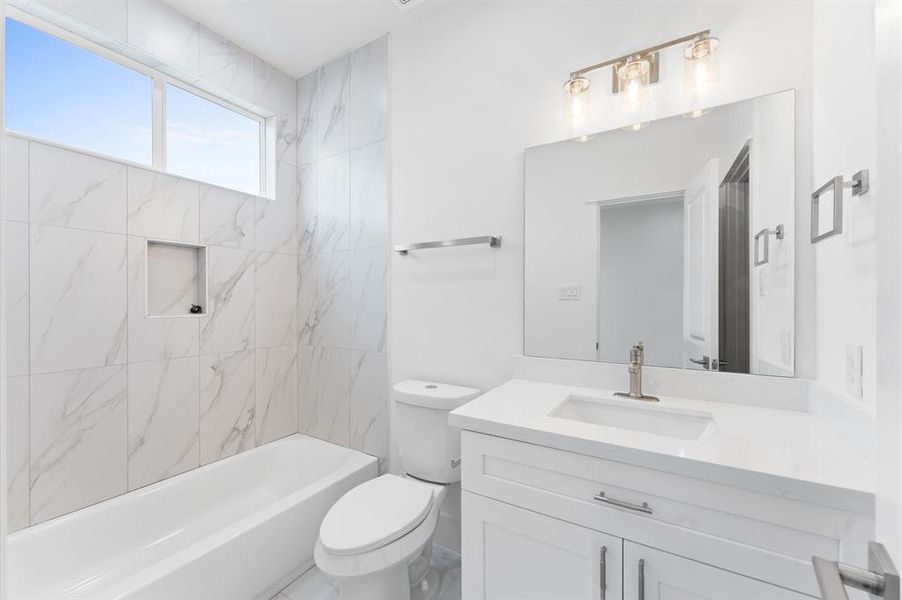 This modern bathroom features elegant marble wall tiles, a sleek vanity with a large mirror, and a bathtub with a built-in niche. Its bright and airy design is complemented by a stylish light fixture and natural light from a high window.