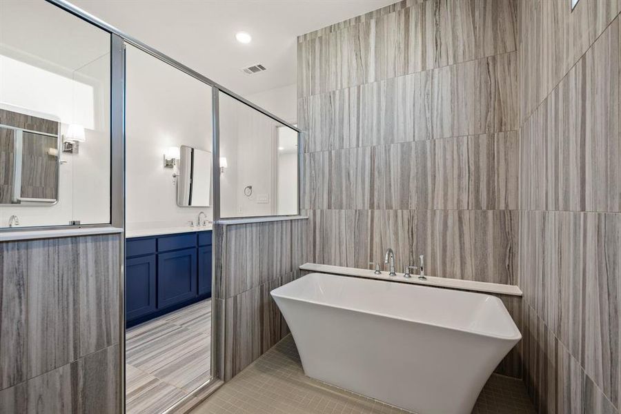 Bathroom featuring tile patterned flooring, vanity, visible vents, a freestanding bath, and tile walls