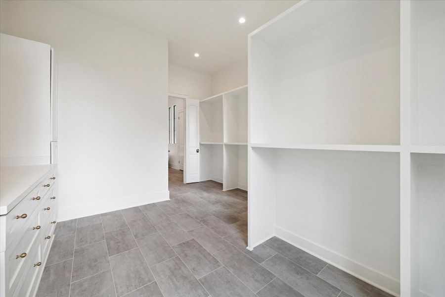 Large walk-in closet with custom onsite built-in shelving, drawer storage, and durable tile flooring.