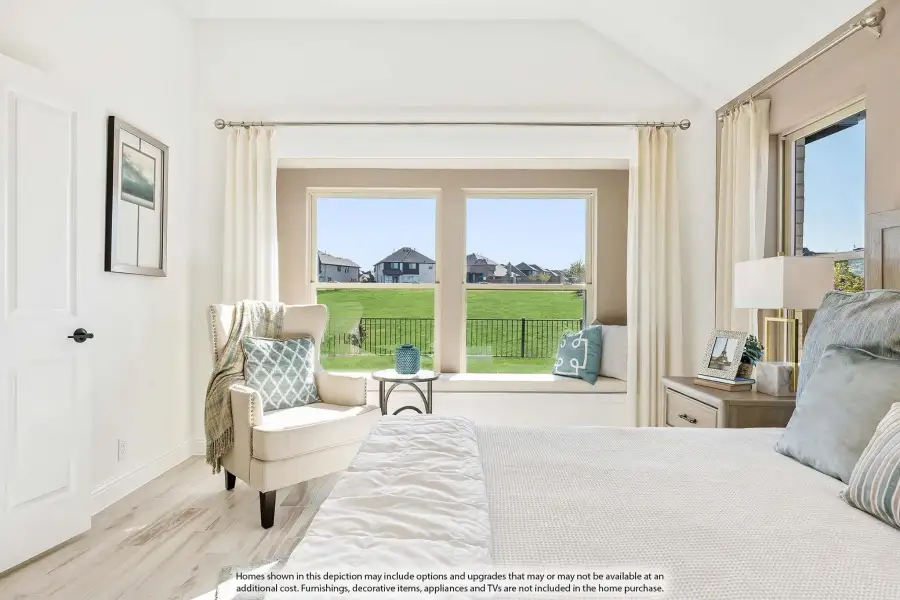 Bright bedroom with vaulted ceiling, window seat, accent chair, and large windows overlooking a green yard