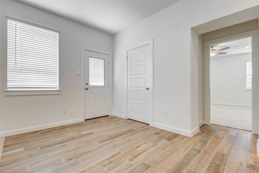 Dining or breakfast area with wood-look tile flooring, a window with blinds, rear door access, nearby storage, and an open passage to the living area. This bright space sits conveniently beside the kitchen and offers a comfortable spot for casual meals or flexible use.