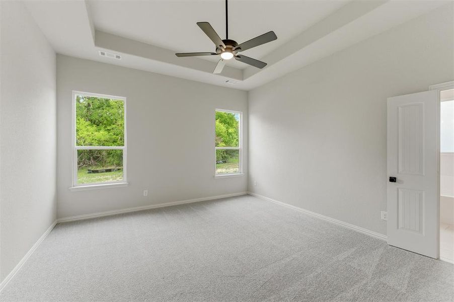 Unfurnished room featuring light carpet, a tray ceiling, and ceiling fan