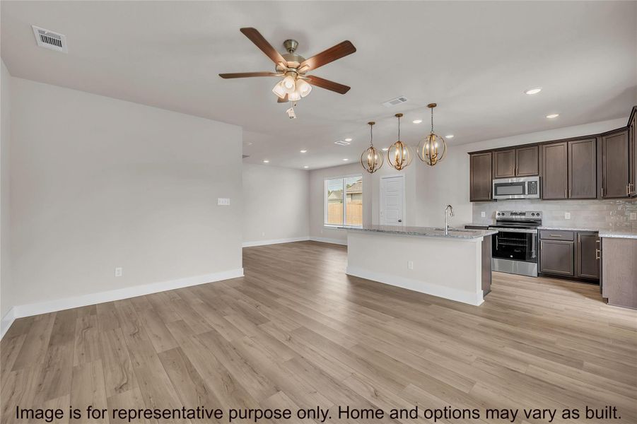 Kitchen featuring stainless steel appliances, open floor plan, dark wood finish cabinets, a ceiling fan, and light stone counters