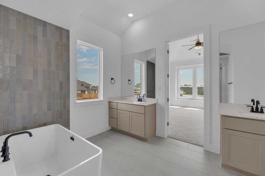Full bath featuring two vanities, a freestanding tub, light tile patterned flooring, lofted ceiling, and recessed lighting Full bath featuring two vanities, a freestanding tub, light tile patterned flooring, lofted ceiling, and recessed lighting