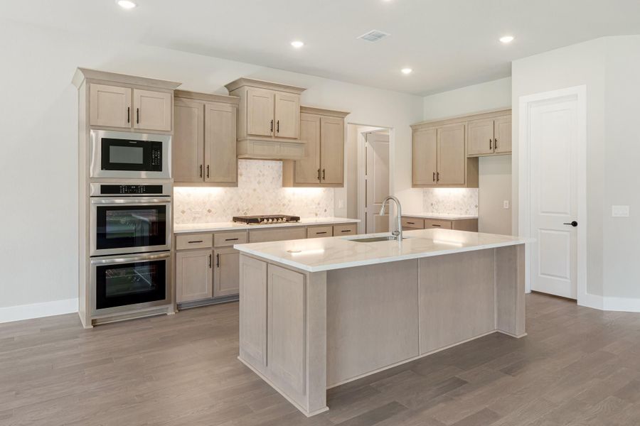 Kitchen with tan cabinets, large center island with sink, double wall ovens, and tile backsplash on wood-look floors