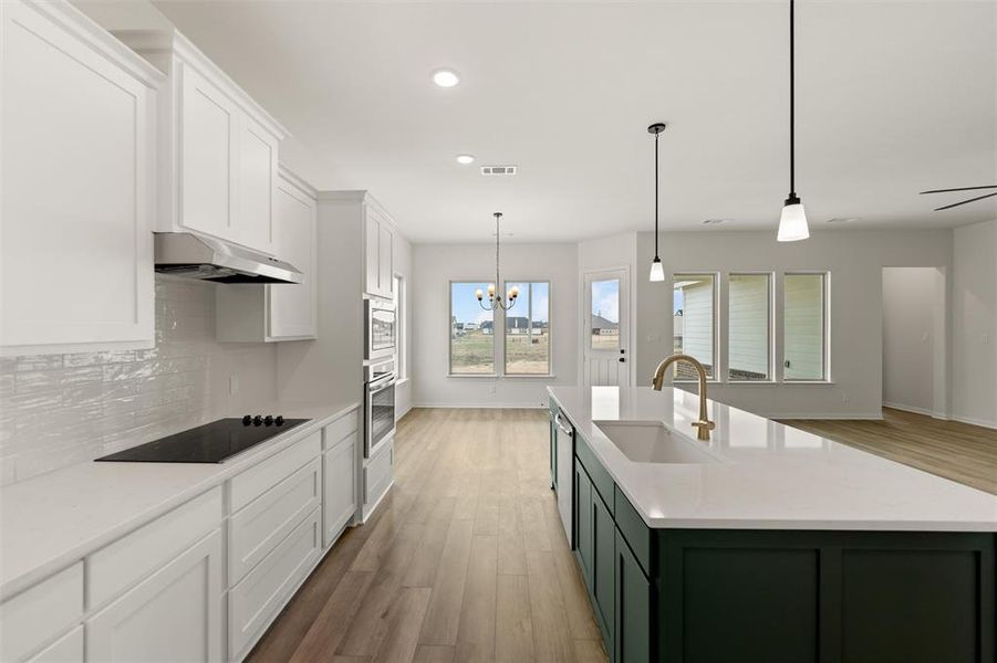 Two tone kitchen featuring dual tone cabinets, suspended lighting, light wood-style flooring, light stone countertops, and stainless steel appliances