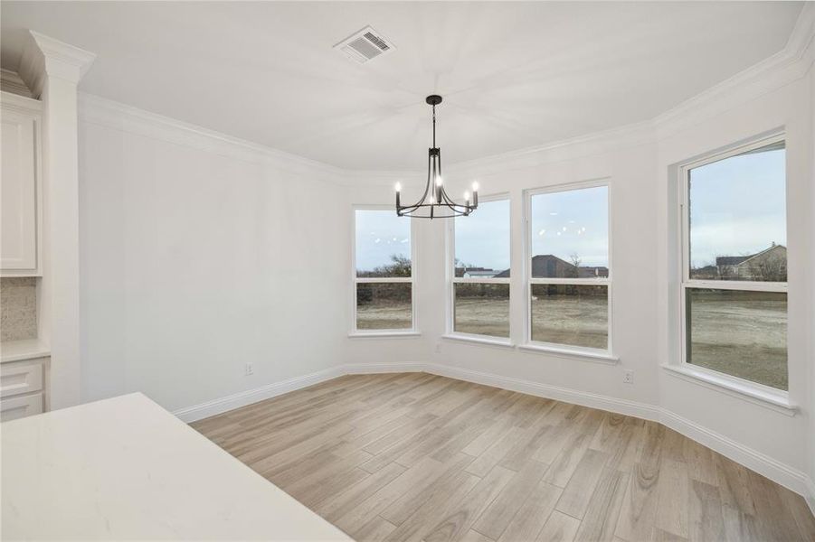 Unfurnished dining area featuring light wood-type flooring, a chandelier, and crown molding